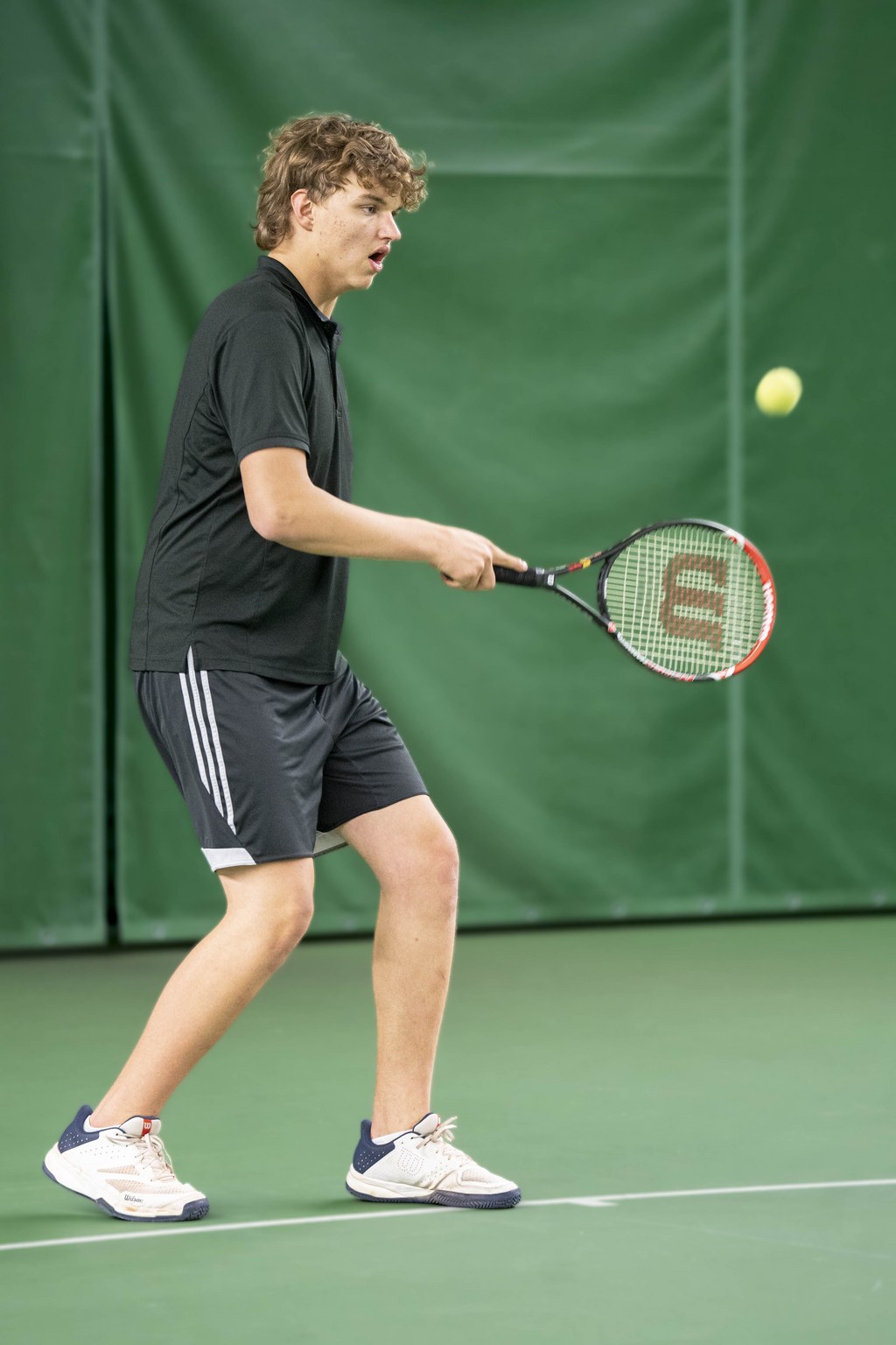 Tennispelaaja syöttämässä tennispalloa keskittyneesti.